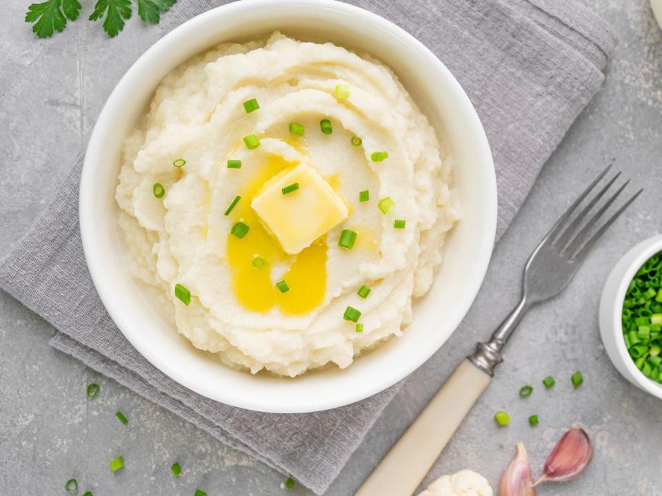 mashed potato with butter and green onions in a white bowl on a gray concrete background. Healthy food.