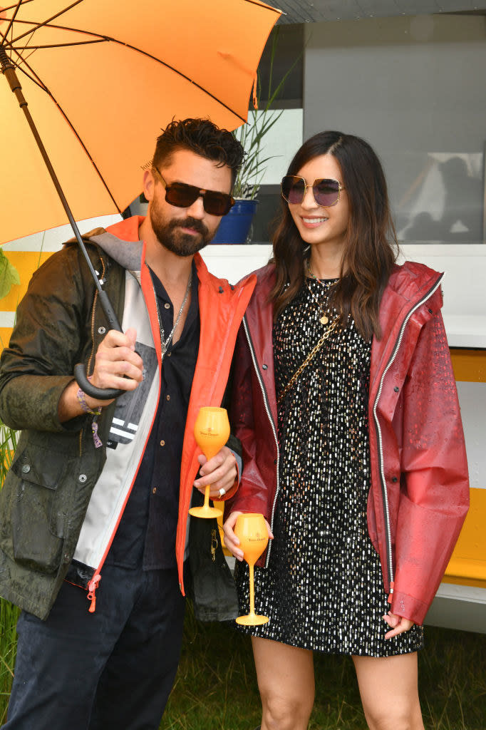 sunglasses on and drinks in hand, Gemma and Dominic pose together under an umbrella