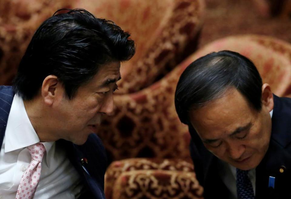 Japan’s prime minister, Shinzo Abe, speaks to chief cabinet secretary, Yoshihide Suga, at the parliament in Tokyo, February 2014.