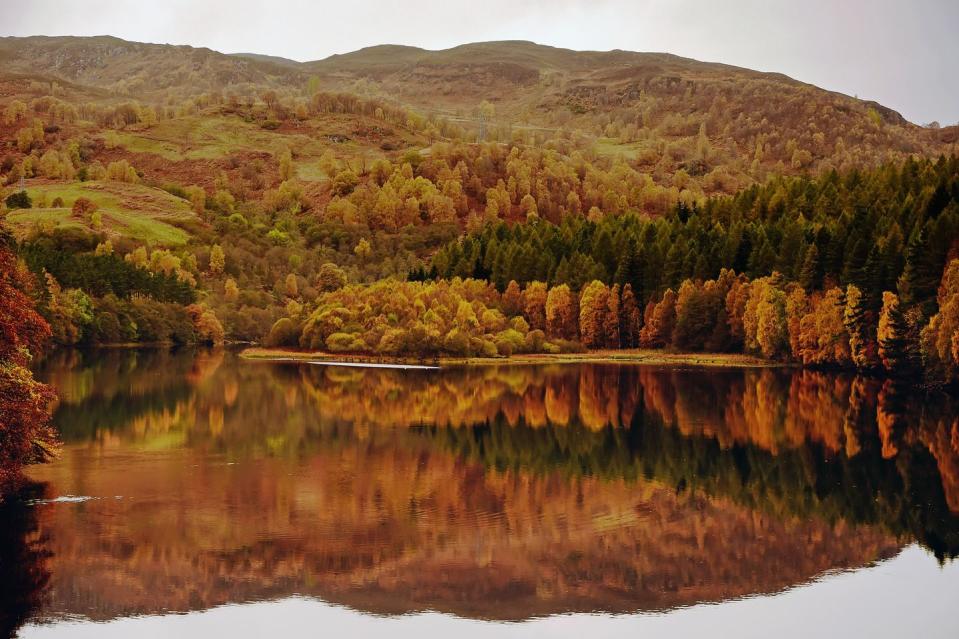 <p>Golden brown trees surround the quiet Lock Fasklally in Pitlochry, Scotland.</p>