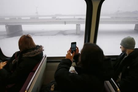 A Metro subway rider takes a picture of the snow-covered Potomac River as a snow falls in Washington January 22, 2016. REUTERS/Jonathan Ernst