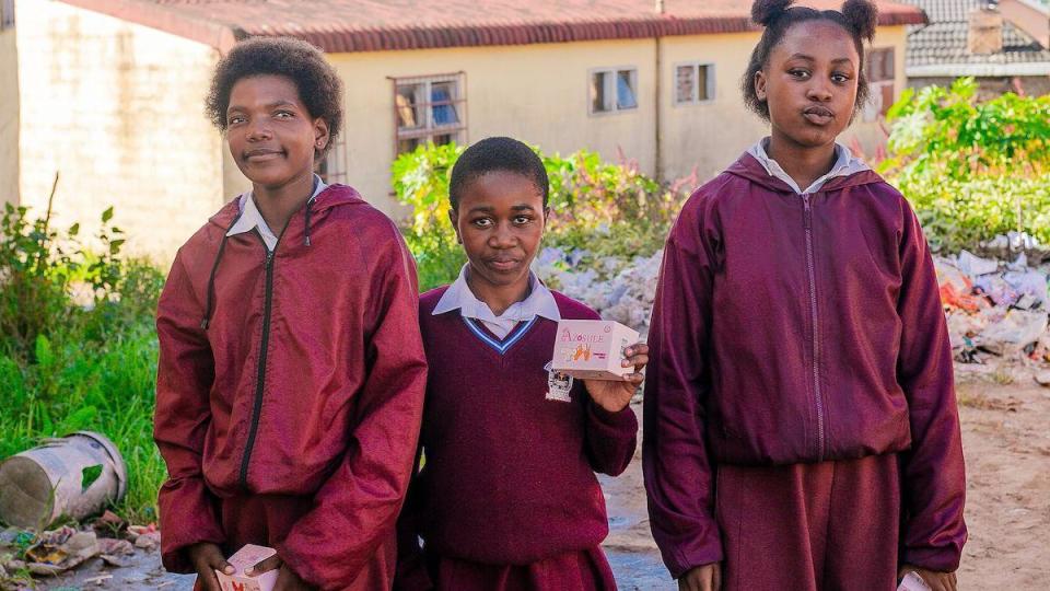 Three girls in school uniforms outside with sanitary pads