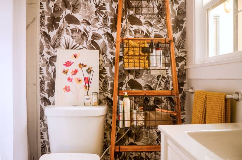 Floral art tops toilet in bathroom with graphic wallpaper.