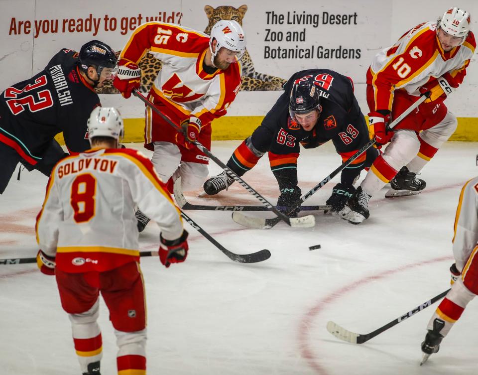 Coachella Valley forward Jacob Melanson (63) reaches out to try to get a hold of the puck along with forward Andrew Poturalski (22) among a pack of Calgary defenders during the third period of Game 3 of the Pacific Division semifinals at Acrisure Arena in Palm Desert, Calif., Wednesday, May 8, 2024.