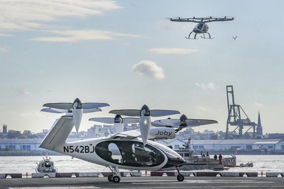 Two style of eVTOL, both with propellers that lift them vertically, with New York Harbor in the background.