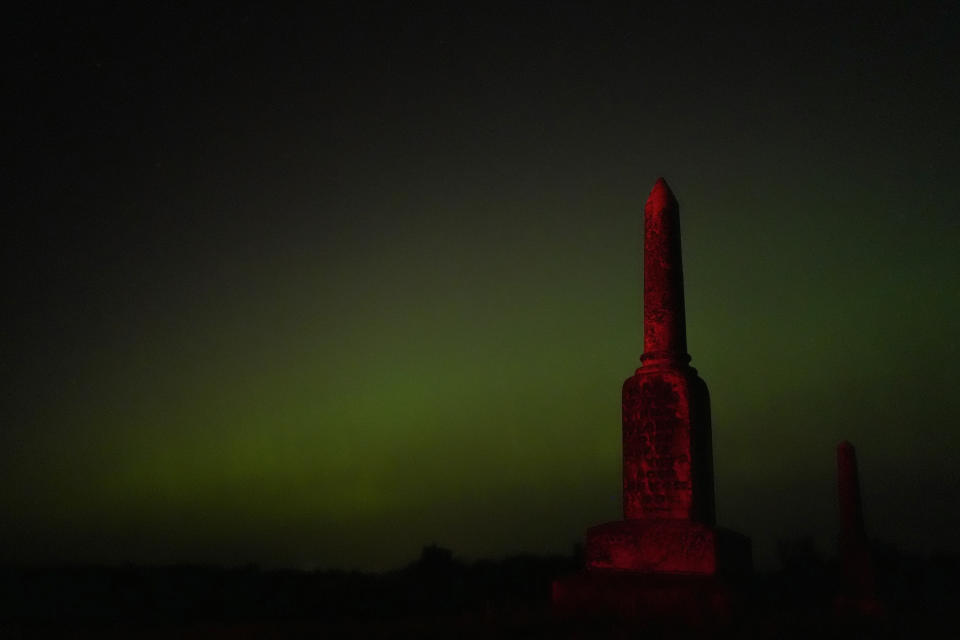 An old tombstone stands against the northern lights at a cemetery early Saturday, May 11, 2024, near Skidmore, Mo. (AP Photo/Charlie Riedel)