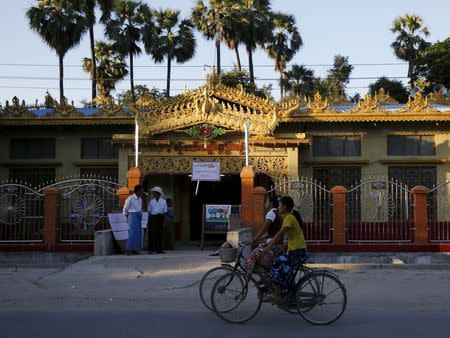 Women cycle past a polling station before tomorrow's general election in Mandalay, Myanmar, November 7, 2015.