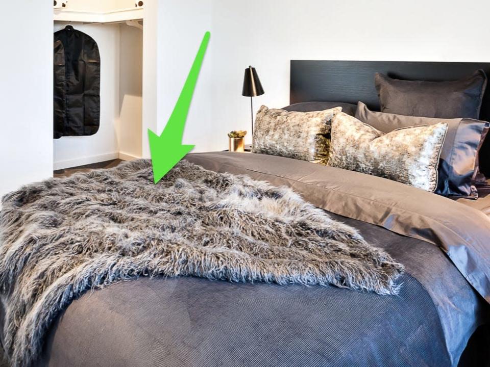 Gray and brown sheets on bed with sequin pillows and a fur throw with green arrow pointing to throw