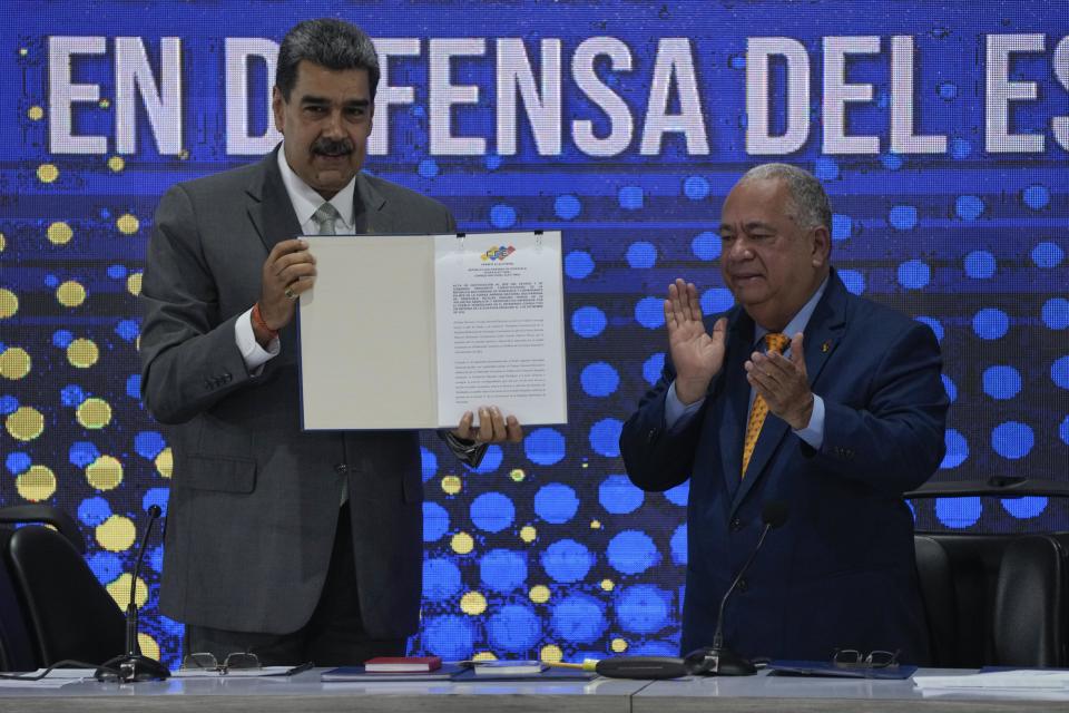 Venezuela's President Nicolas Maduro, left, shows the referendum notification act given to him by National Electoral Council President Elvis Hidrobo Amoroso, during the notification ceremony for the referendum about the future of a disputed territory with Guyana, in Caracas, Venezuela, Monday, Dec. 4, 2023. (AP Photo/Ariana Cubillos)