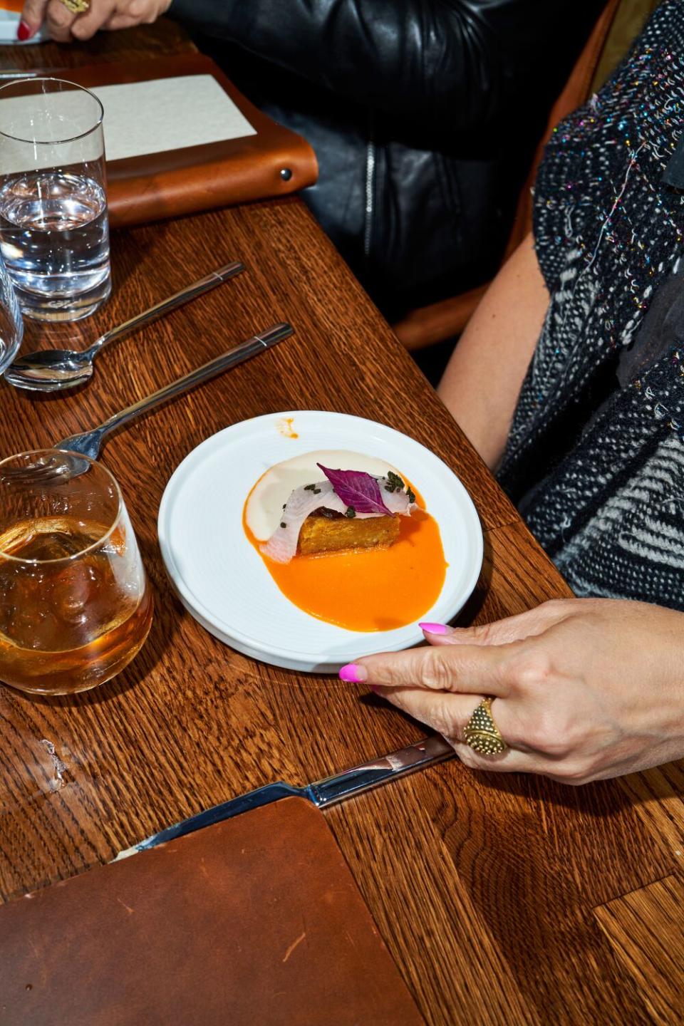 A white plate containing a rectangular chunk of potatoes draped in kanpachi and drizzled in sauce.