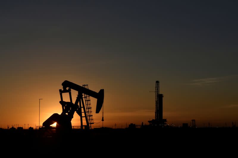 A pump jack operates in front of a drilling rig at sunset in an oil field in Texas