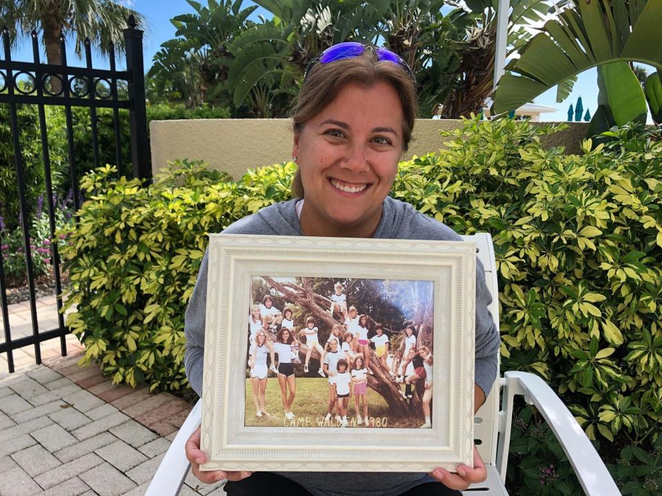 In this June 22, 2020, photo provided by Shaye Spector, Camp Walden Director Robyn Spector holds a group photo from one of her first summers at camp. Spector, 48, would have been spending her 40th summer at Camp Walden, a co-ed sleepaway camp near Lake George in Diamond Point, N.Y. (Shaye Spector via AP)