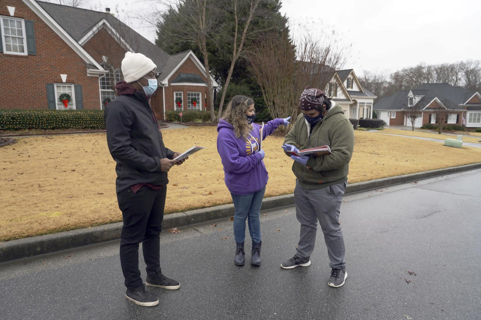Robert Campbell, Stephanie Lopez-Burgus and Graco Hernandez Valenzuela, from left, pause while canvassing a neighborhood for the Working Families Party regarding the U.S. Senate races, Wednesday, Dec. 16, 2020, in Lawrenceville, Ga. (AP Photo/Tami Chappell)
