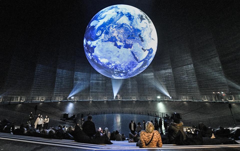 FILE - In this Thursday, Oct. 7, 2021 file photo, visitors watch a giant earth installation at the exhibition "The Fragile Paradise" inside the former industrial gas storage facility "Gasometer" in Oberhausen, Germany. The 2021 U.N. climate summit in Glasgow renews an urgent question to the international community: Can the world come together to confront the common enemy of global warming before it’s too late? (AP Photo/Martin Meissner, File)