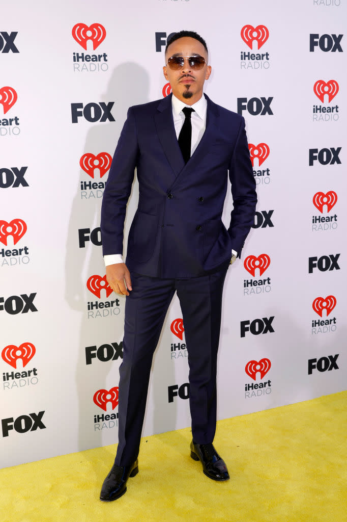 Person in a tailored suit with a tie, posing at an event with iHeartRadio and FOX logos in the background