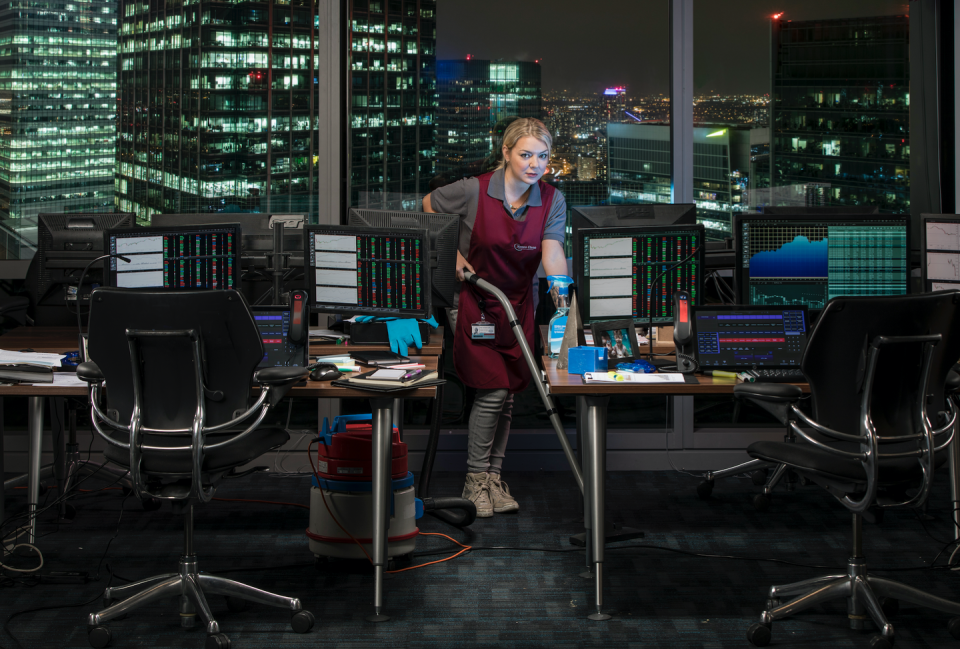 cleaning up on itv, sheridan smith in an apron with a vacuum cleaner in a london high rise office