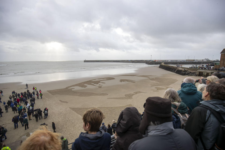 <p>People gather around a drawing of war poet Wilfred Owen on Sunny Sands beach in Folkestone, during the Pages of the Sea commemorative event. (Steve Parsons/PA via AP) </p>