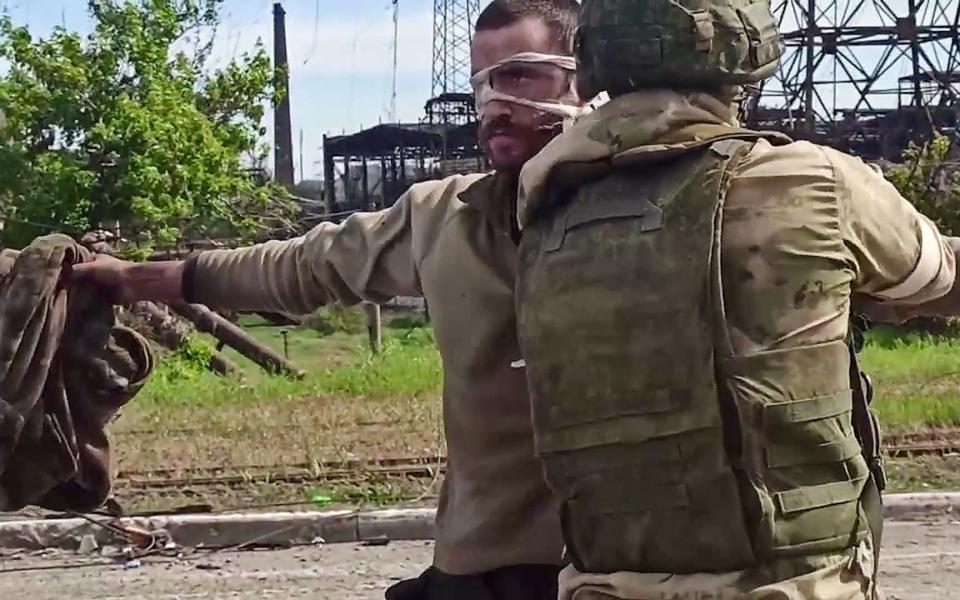 A Ukrainian soldier is searched by a Russian military official after leaving the besieged Azovstal steel plant in Mariupol - AFP