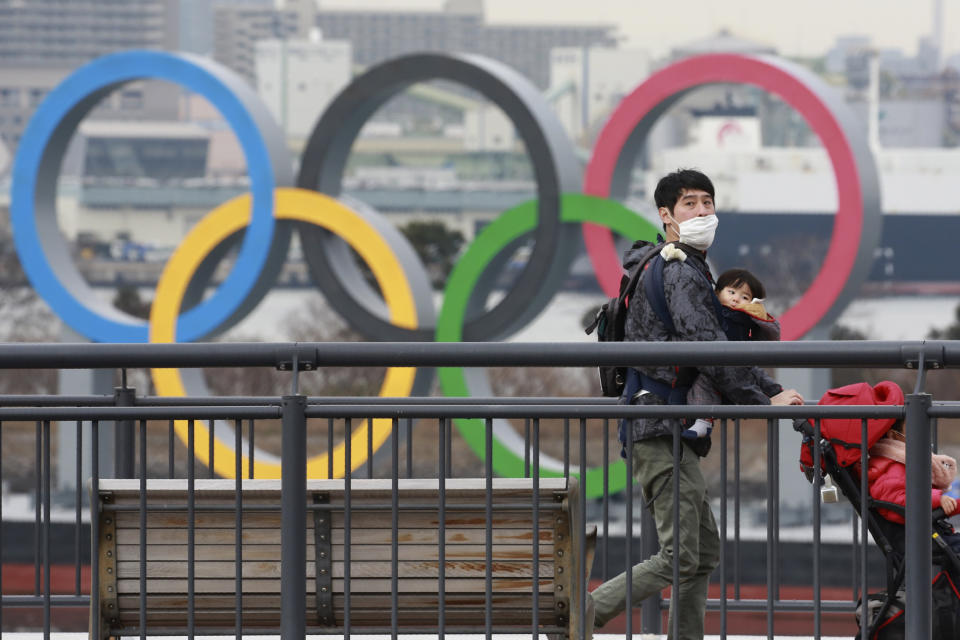 People wearing face masks to protect against the spread of the coronavirus walk on the Odaiba waterfront as Olympic rings are seen in the background in Tokyo, Tuesday, Jan. 26, 2021. (Photo: AP Photo/Koji Sasahara)