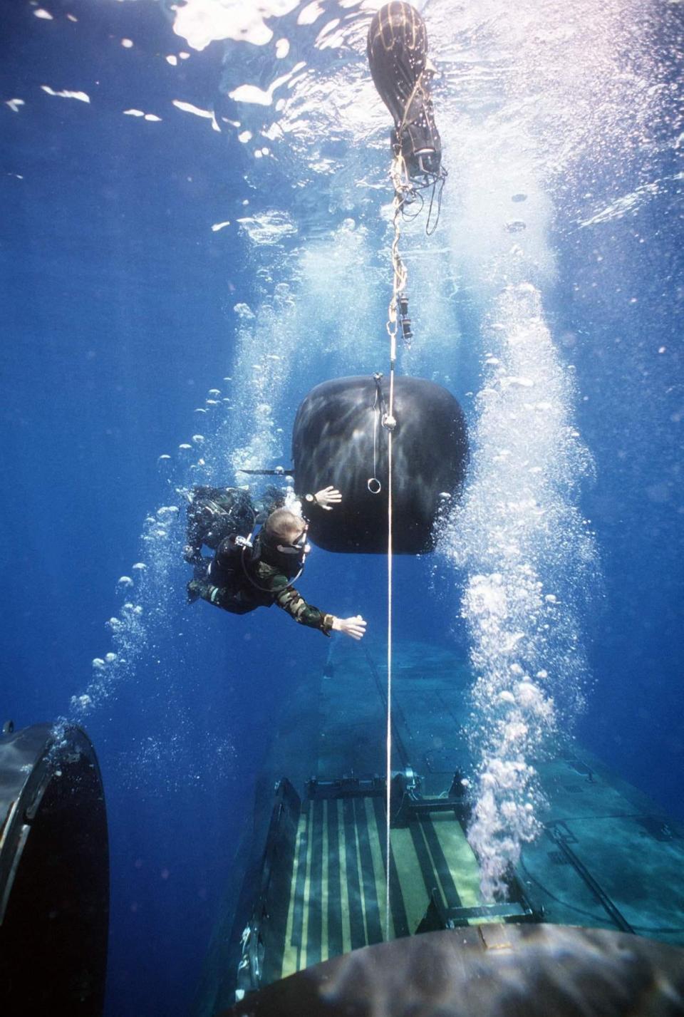 Dry deck shelter crewmen swim down the tether line to the DDS on board the now-retired nuclear-powered submarine USS Kamehameha