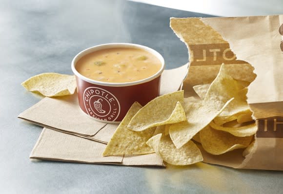 A cup of Chipotle queso next to a bag of tortilla chips