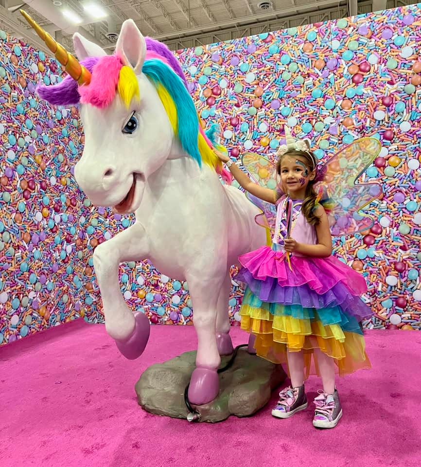 A girl poses next to unicorn animatronic Sprinkles.