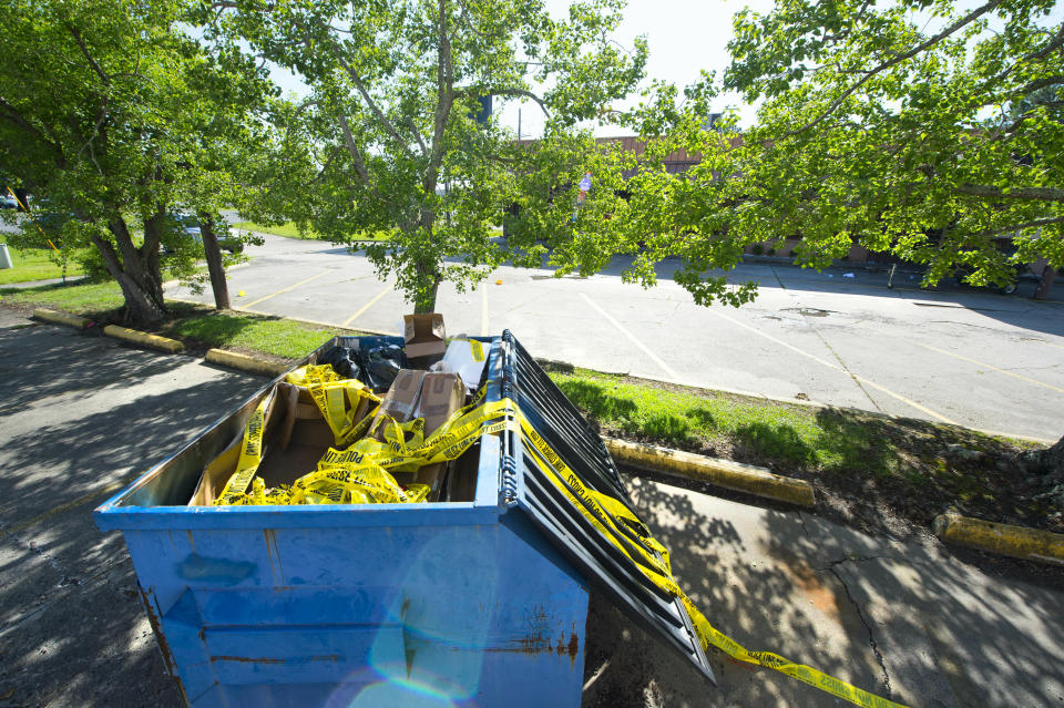 Crime scene tape lies discarded in a next-door parking lot dumpster, seen Saturday, June 29, 2019, near Stadium Ultralounge & Bar, background right, obscured by trees, where multiple people were injured in a shooting earlier in the day, in Baton Rouge, La. (Travis Spradling/The Advocate via AP)