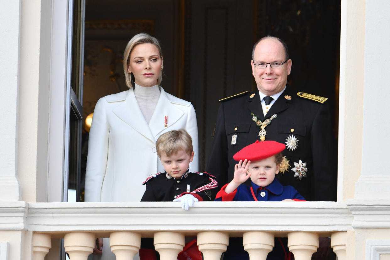 Charlene in a white coat, Albert in a navy regal outfit and their two young children wave from a balcony. (Stephane Cardinale / Corbis via Getty Images)