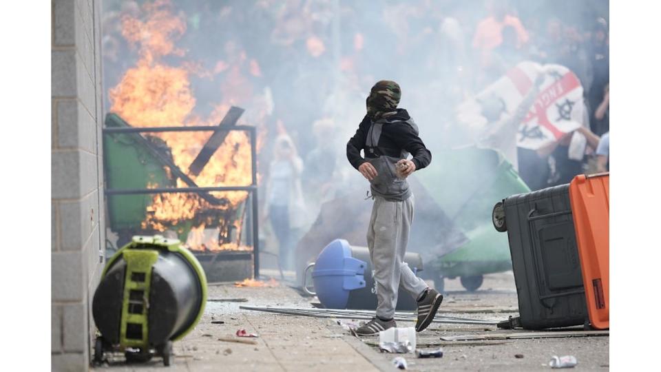 A young rioter surrounded by fires and overturned bins