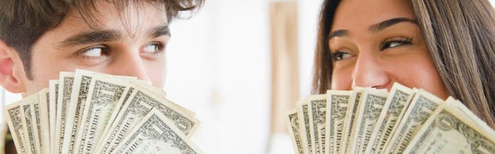 A couple fanning money in front of their faces and smiling at one another