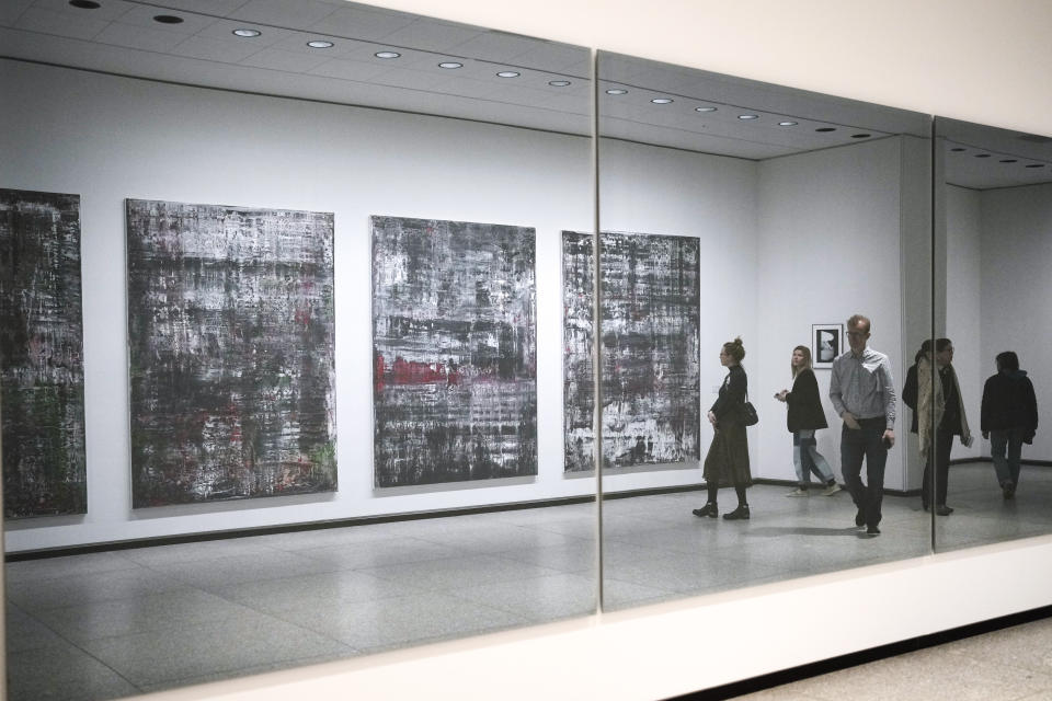 People reflected in a mirror oposite of the 'Birkenau' paintings in a new exhibition with art works of German artist Gerhard Richter at the New National Gallery in Berlin, Germany, Friday, March 31, 2023. Richter's foundation gave on permanent loan 100 works of the artist to the New National Gallery where they will be shown in the permanent exhibition. (AP Photo/Markus Schreiber)