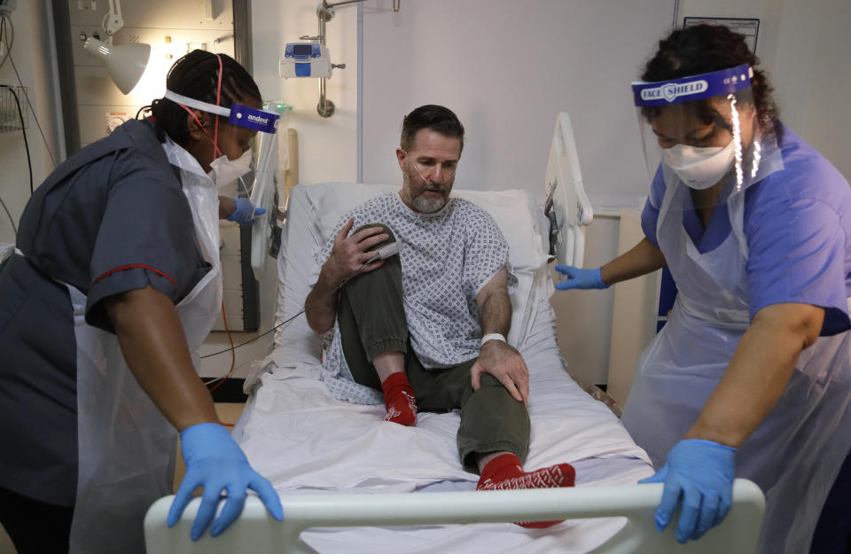 Felicia Kwaku, Associate Director of Nursing, left, and Anna Castellano, Matron, right, help recovering COVID-19 patient Justin Fleming out of bed to try to walk again on the Cotton ward at King's College Hospital in London, Wednesday, Jan. 27, 2021. Fleming is one of more than 37,000 coronavirus patients being treated now in Britain's hospitals, almost double the number of the spring surge. King's College Hospital, which sits in a diverse, densely populated area of south London, had almost 800 COVID-19 patients earlier this winter. (AP Photo/Kirsty Wigglesworth, Pool)