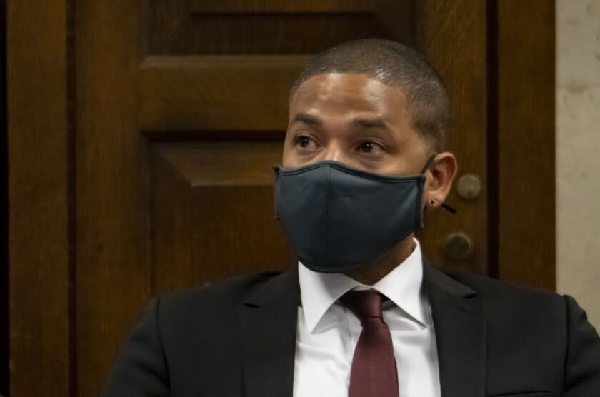 A man with a shaved head wearing a black face mask and a black suit