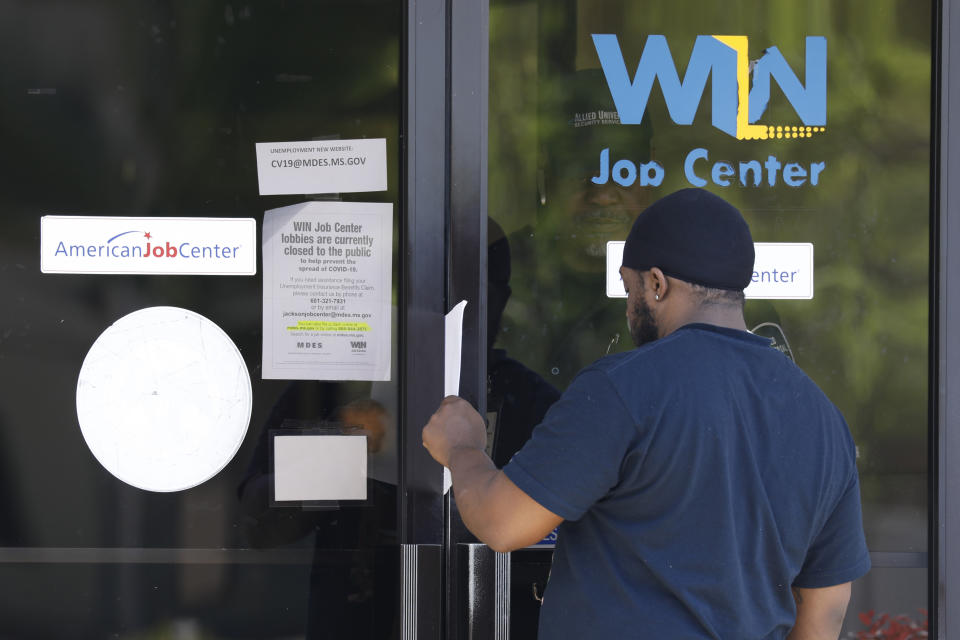 Tyrone Keoton Jr., is handed an unemployment benefit application form by a security guard behind the glass doors of this state WIN Job Center in north Jackson, Miss., Thursday, April 2, 2020. The job centers lobbies are closed statewide to prevent the spread of COVID-19. The agency encourages residents to apply for their benefits on line, however, the system has been stressed by the large numbers of applicants. The local job centers are making paper unemployment applications available and applicants are filling them out and pushing them back through the mail slots or doors as well as they can. (AP Photo/Rogelio V. Solis)