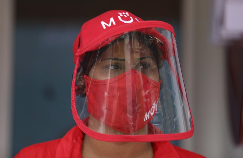 An employee, wearing a protective mask and face shield, stands at the entrance of a MUY restaurant, a Colombian fast food chain that is planning to turn its branches into automated restaurants, in Bogota, Colombia, Thursday, Aug. 13, 2020. The chain has opened its first “contactless store” in a commercial district of Bogota, where many restaurants have been forced to shut down because of a ban on sit-down dining. (AP Photo/Fernando Vergara)