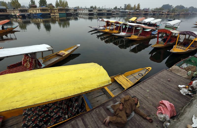 A man sleeps next to parked "Shikaras" or boats on the banks of Dal Lake in Srinagar