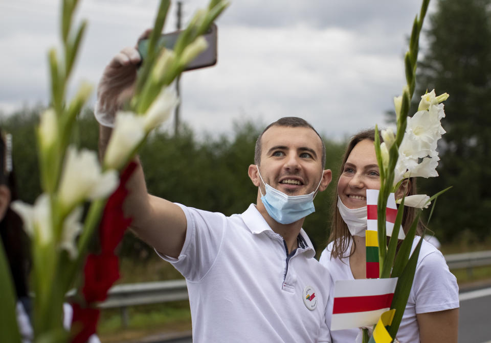 Supporters of Belarus opposition from Lithuania hold historical Belarusian flags and takes a selfie during the "Freedom Way", a human chain of about 50,000 strong from Vilnius to the Belarusian border, during a protest near Medininkai, Lithuanian-Belarusian border crossing east of Vilnius, Lithuania, Sunday, Aug. 23, 2020. In Aug. 23, 1989, around 2 million Lithuanians, Latvians, and Estonians joined forces in a living 600 km (375 mile) long human chain Baltic Way, thus demonstrating their desire to be free. Now, Lithuania is expressing solidarity with the people of Belarus, who are fighting for freedom today. (AP Photo/Mindaugas Kulbis)