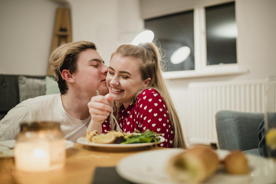 young adults having dinner at home while one tries to kiss the others cheek