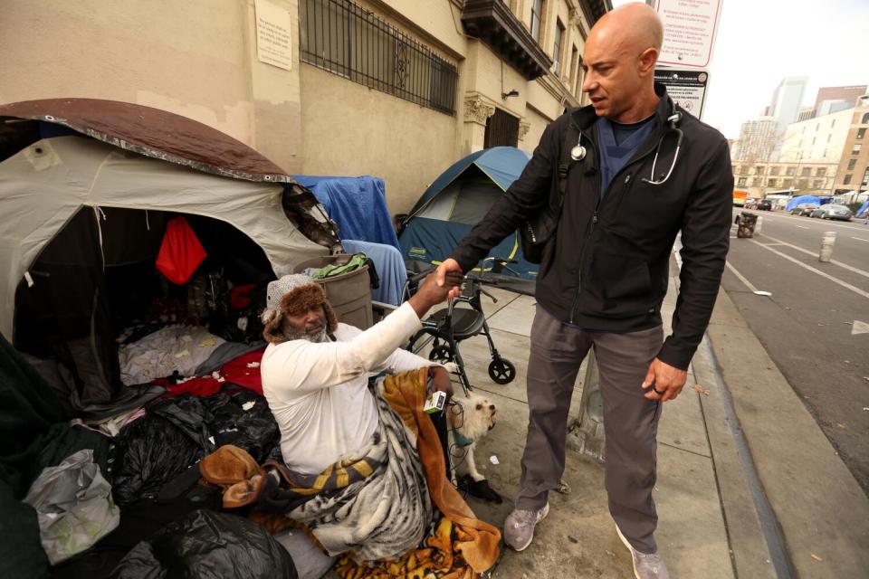 A man in front of a tent shakes hands with another man.