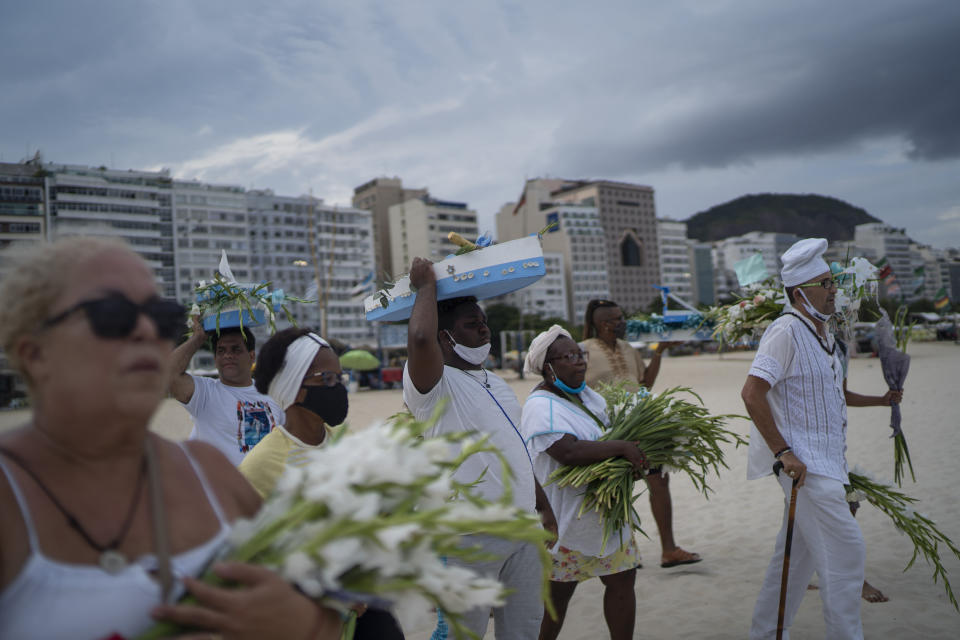 Worshippers with offerings for Yemanja, goddess of the sea, walk on Copacabana beach during an an Afro-Brazilian ceremony that is part of traditional New Year's celebrations to plea for relief from the new coronavirus pandemic and asks for a better new year, in Rio de Janeiro, Brazil, Tuesday, Dec. 29, 2020. (AP Photo/Lucas Dumphreys)