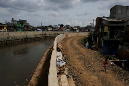 A child runs next to concrete walls that were built to prevent flooding at Ciliwung river banks at Jatinegara district in Jakarta, Indonesia, December 29, 2016. Picture taken December 29, 2016. REUTERS/Beawiharta