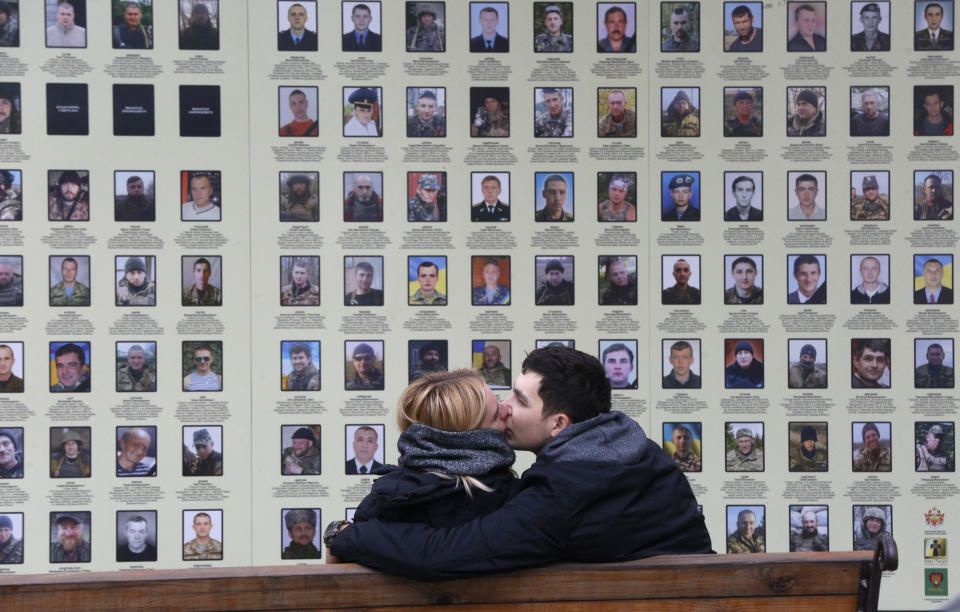 FILE- A couple shares a kiss at a memorial wall with photos of servicemen killed in the conflict with pro-Russian separatists in the country's east, in Kyiv, Ukraine, Tuesday, Nov. 19, 2019. More than 100,000 Russian troops are massed along the Ukrainian border in 2022, preparing for a possible invasion. Vladimir Putin's Russia has perfected the art of flouting the rules, whether the venue is the Olympic arena, international diplomacy or meddling in other countries' elections from the comfort of home. And it has suffered little consequence for its actions. (AP Photo/Efrem Lukatsky, File)