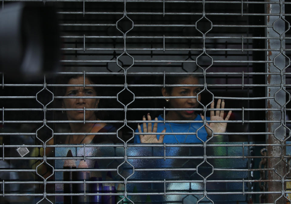 A couple of women look out from the shuttered window of a business as Venezuela's opposition leader and self proclaimed president Juan Guaido, leads a rally in Maracay, Venezuela, Friday, April 26, 2019. The Trump administration has added Venezuelan Foreign Minister Jorge Arreaza to a Treasury Department sanctions target list as it increases pressure on Guaido's opponent, embattled President Nicolas Maduro. (AP Photo/Fernando Llano)