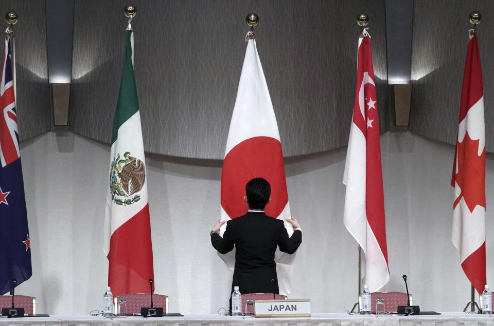 A staff adjusts the Japanese flag prior to a joint press conference of the Comprehensive and Progressive Trans-Pacific Partnership (CPTPP) in Tokyo, Saturday, Jan. 19, 2019. Trade ministers of a Pacific Rim trade bloc are meeting in Tokyo, gearing up to roll out and expand the market-opening initiative. (AP Photo/Eugene Hoshiko)