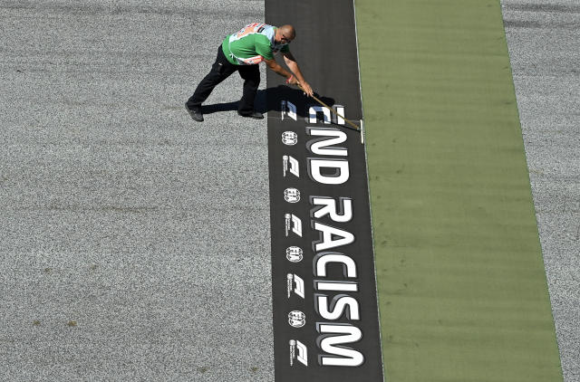 A worker prepares a sticker reading 'End Racism' on the track before the Austrian Formula One Grand Prix race at the Red Bull Ring racetrack in Spielberg, Austria, Sunday, July 5, 2020. (Joe Klamar/Pool via AP)