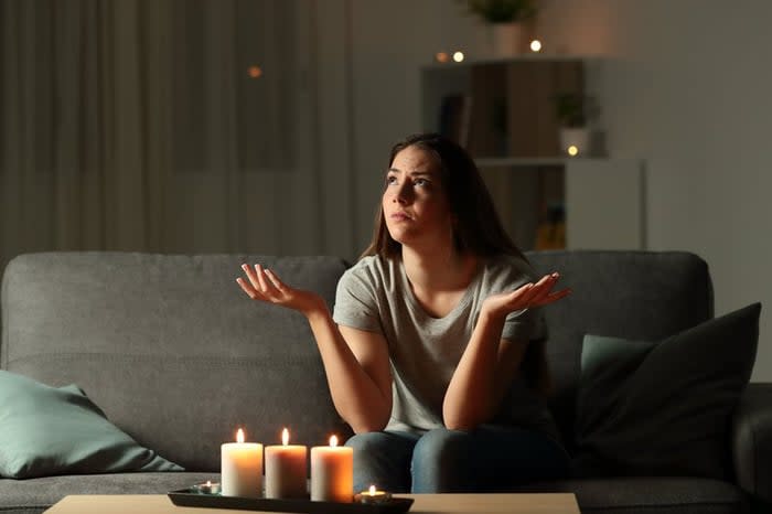 A frustrated person sitting on the couch in a power outage with lit candles on the coffee table.