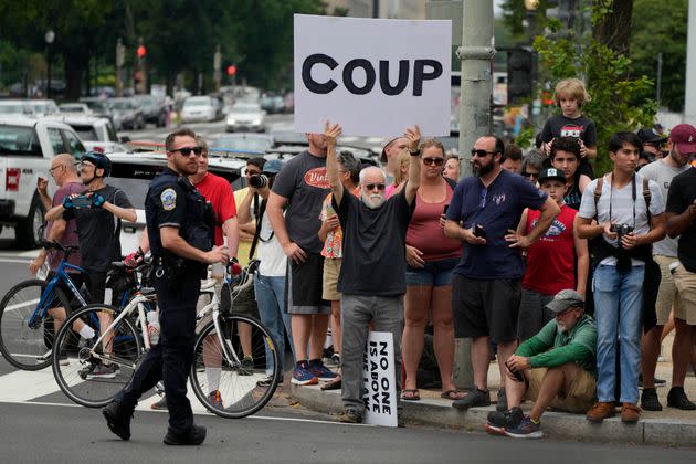 People gather, one with a sign that reads 