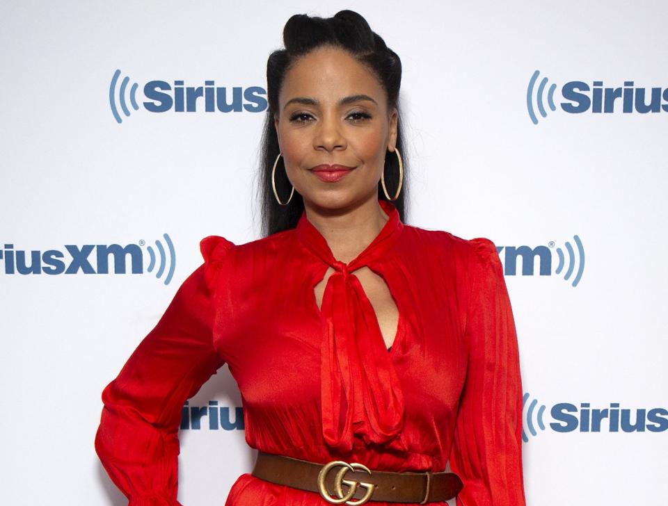 Sanaa wears a red dress with a keyhole neckline and brown Gucci belt
