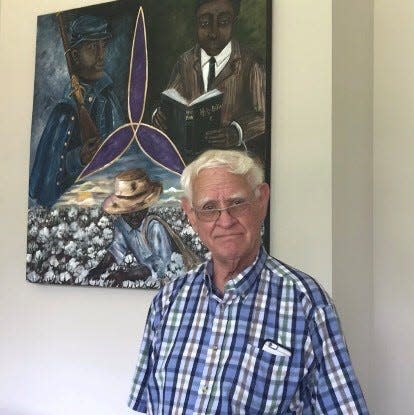 Richard Martin, an opponent of reparations whose family has roots in northern Alabama as old as the McConnell family, stands in front of at the historic black Trinity High School depicting a black slave, soldier and student.