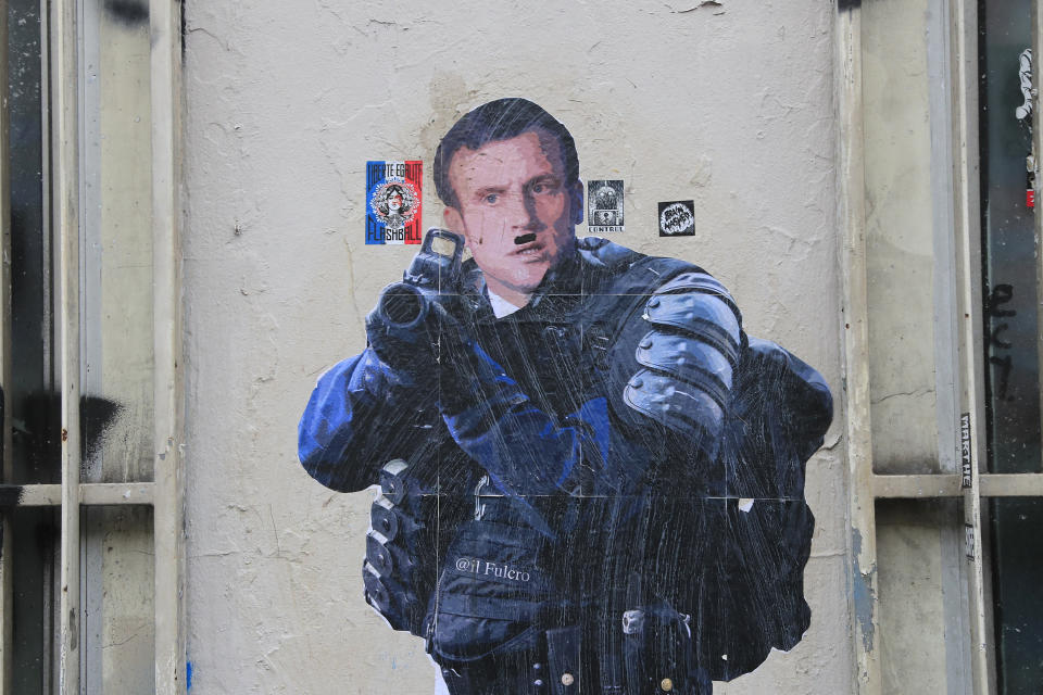 A graffiti shows French President Emmanuel Macron dressed like a riot police officer and aiming at protesters during a demonstration Thursday, Dec. 19, 2019 in Paris. Traffic improved slightly on French trains Thursday as nationwide strikes over the government's retirement reform entered a 15th day and small signs of progress emerged in negotiations with unions. (AP Photo/Michel Euler)